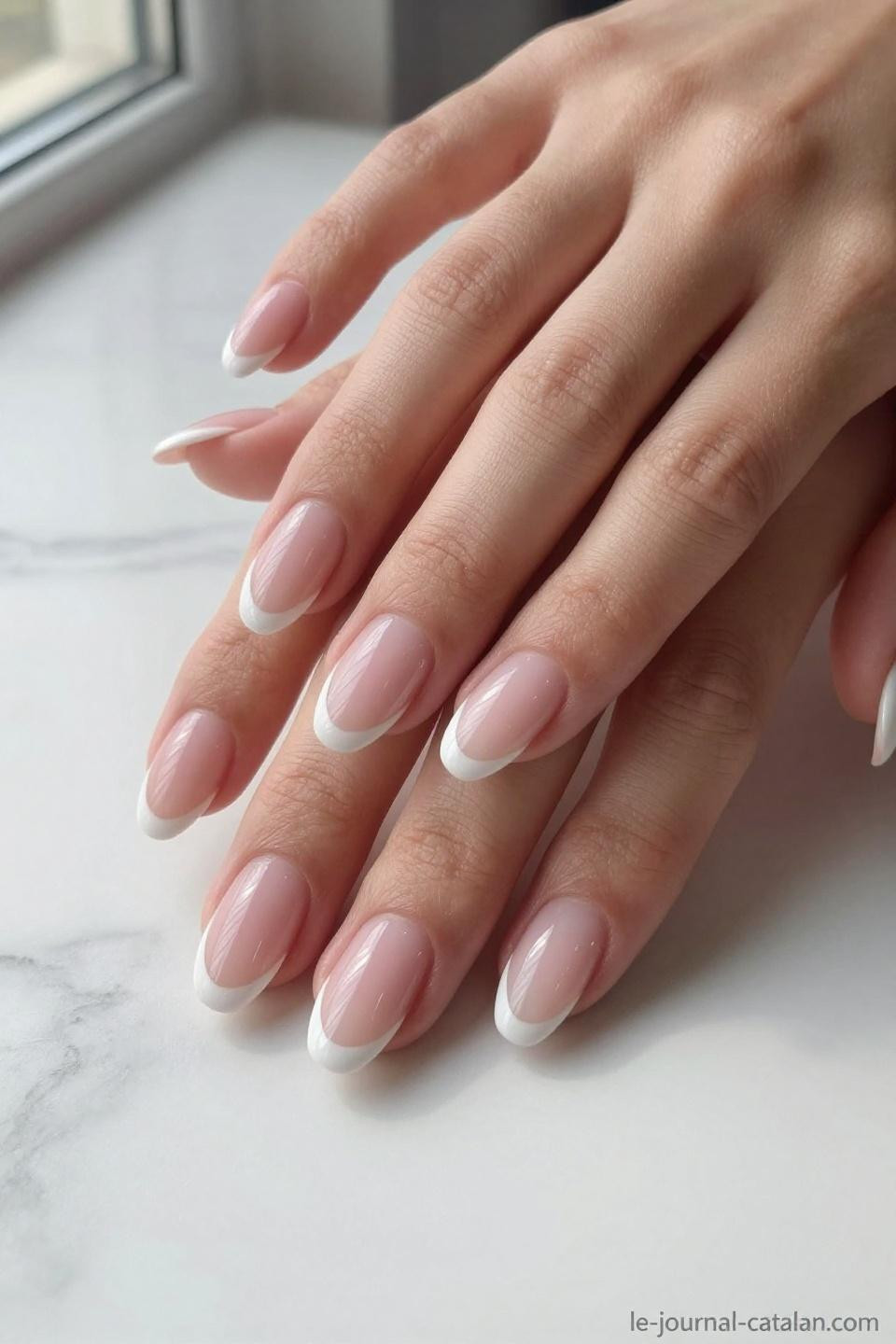 Almond French tips with translucent beige base on marble surface with luxury beauty styling