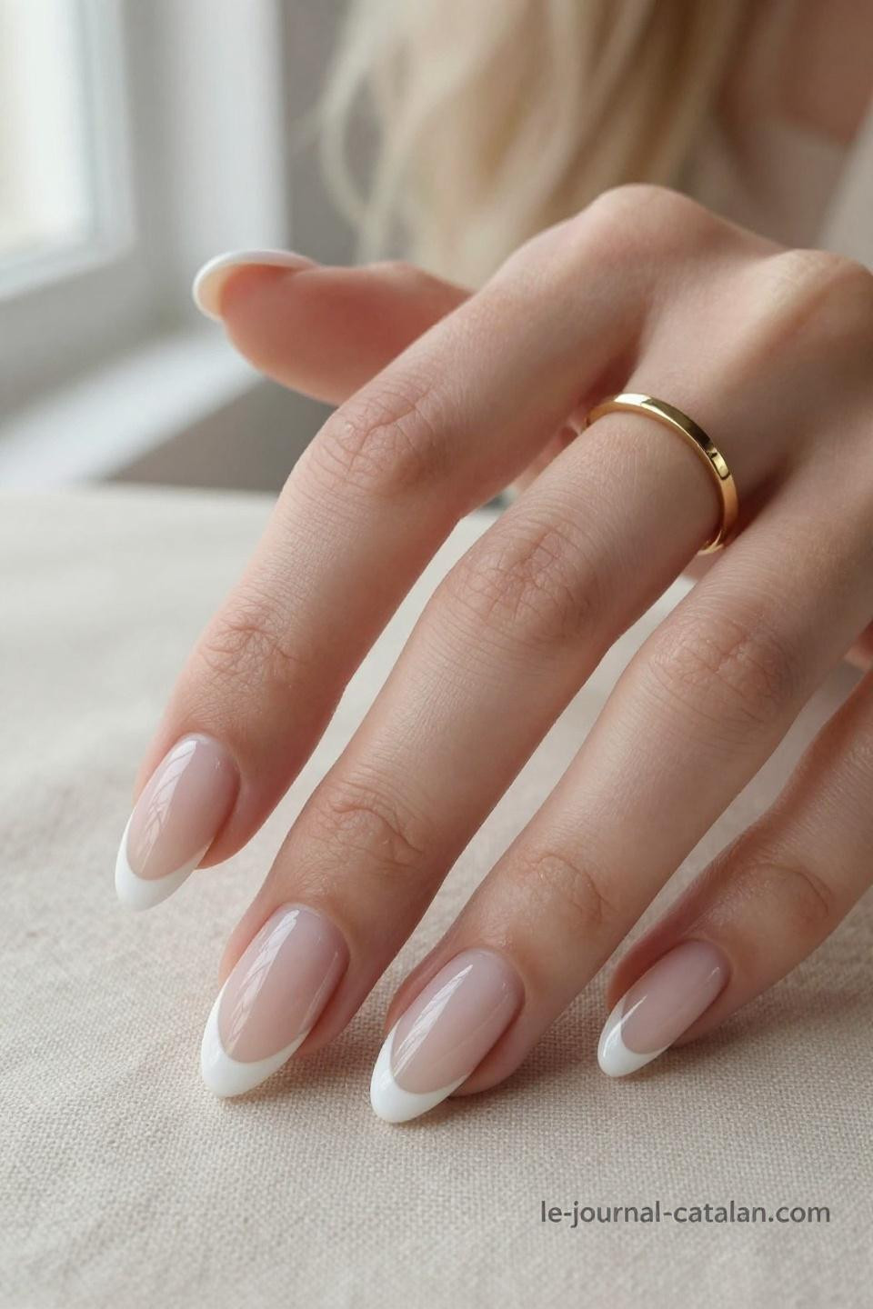 Almond French tip nails with natural pink base and pristine white tips on porcelain hands against cream linen backdrop