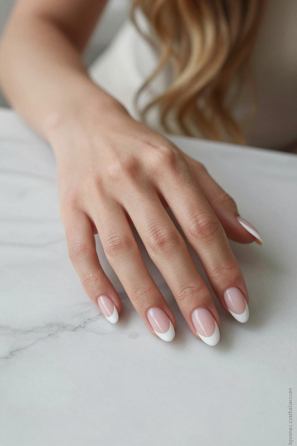 Timeless French manicure on almond nails against white Carrara marble creating sophisticated beauty composition