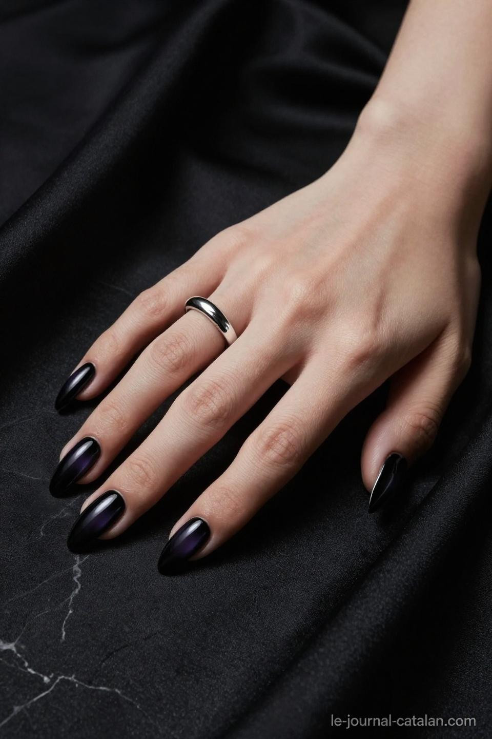 dark black nails in almond shape with glossy gel against black marble and silk fabric