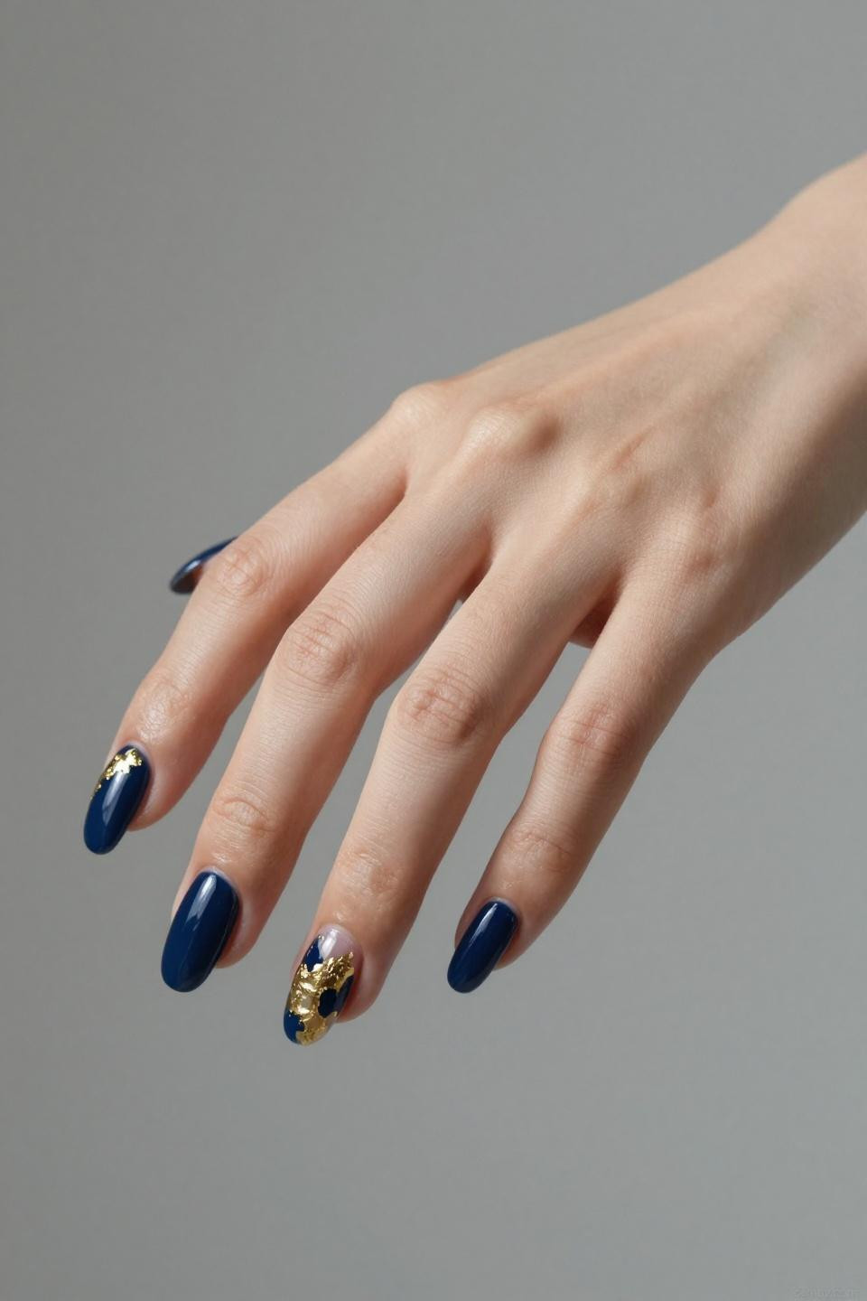 Navy Blue Nails with gold foil accent on almond shaped nails against gray backdrop