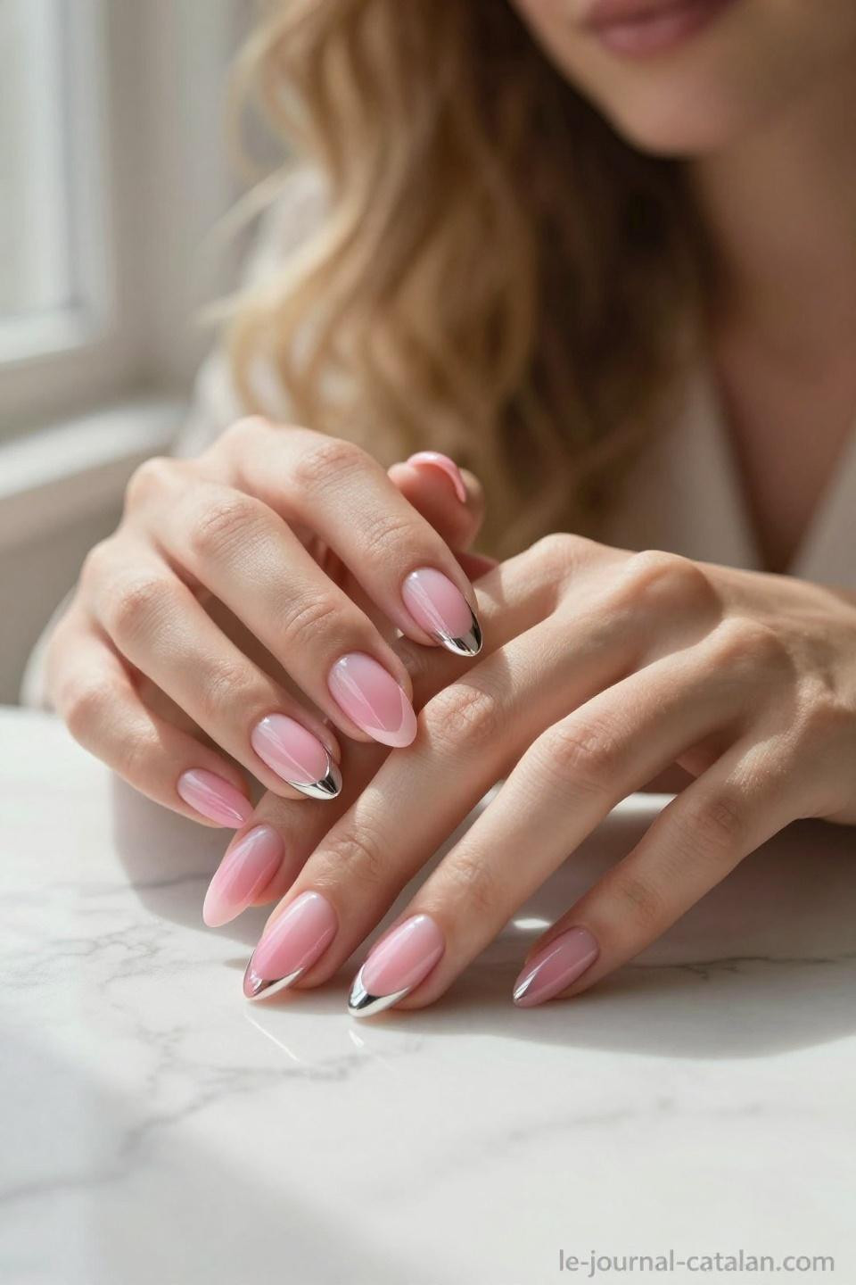 Light pink almond nails with chrome accent details in natural window light