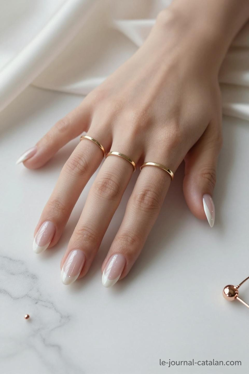 Short almond nails with champagne shimmer nude and gold ring accents on marble